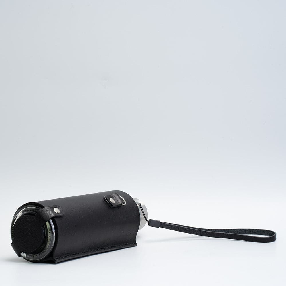 Leather water bottle holder featuring a glass bottle, bamboo lid, and adjustable strap, designed for stylish hydration on the go.