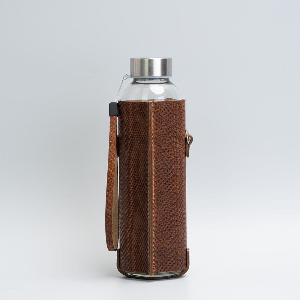 Leather water bottle holder featuring a glass bottle, bamboo lid, and adjustable strap, designed for stylish hydration on the go.