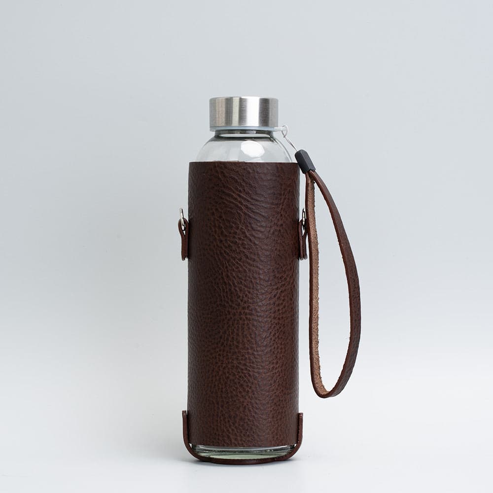 Leather water bottle holder featuring a glass bottle, bamboo lid, and adjustable strap, designed for stylish hydration on the go.