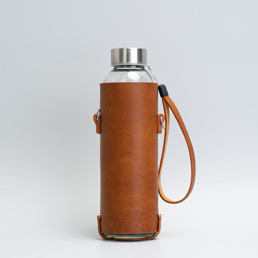 Leather water bottle holder featuring a glass bottle, bamboo lid, and adjustable strap, designed for stylish hydration on the go.
