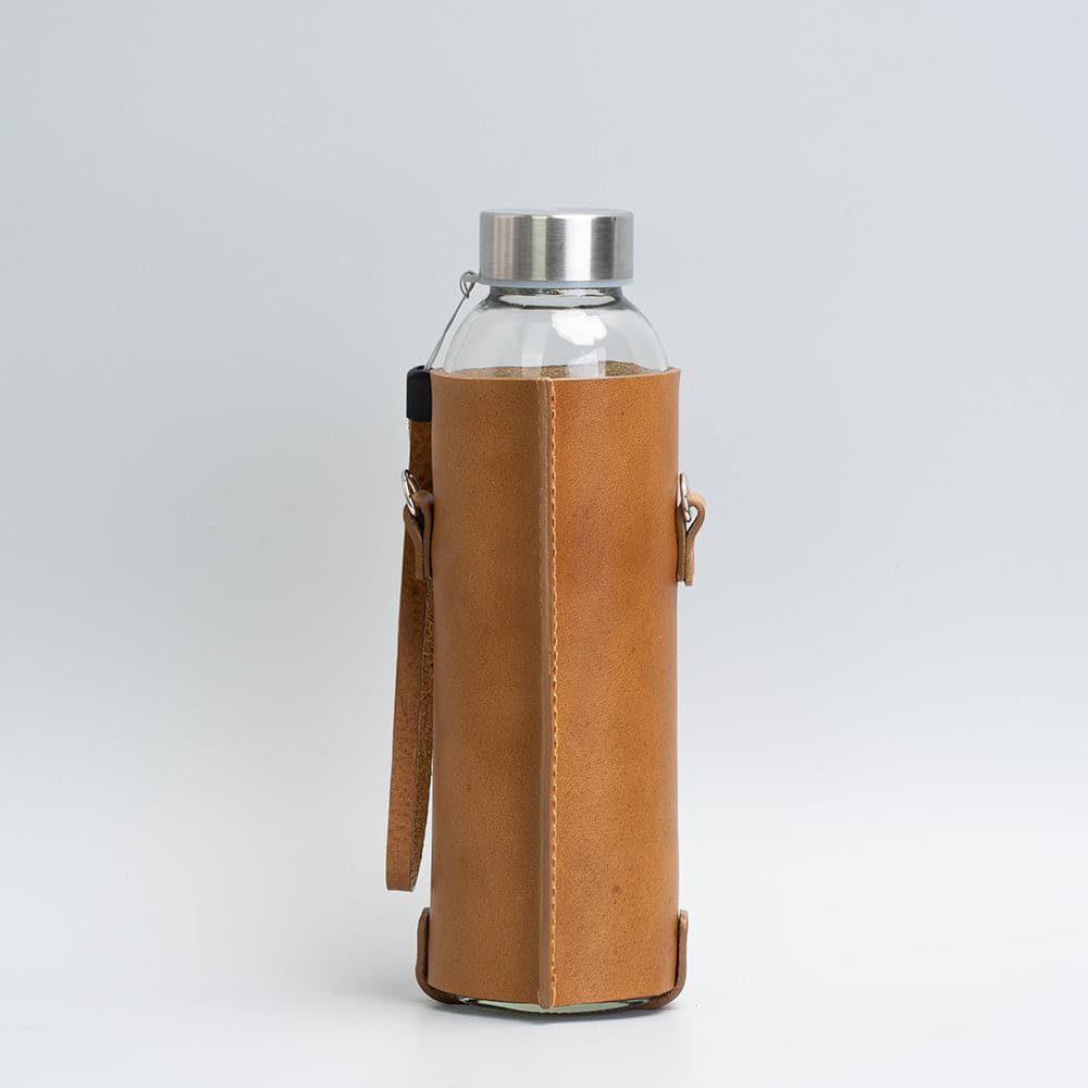 Leather water bottle holder featuring a glass bottle, bamboo lid, and adjustable strap, designed for stylish hydration on the go.