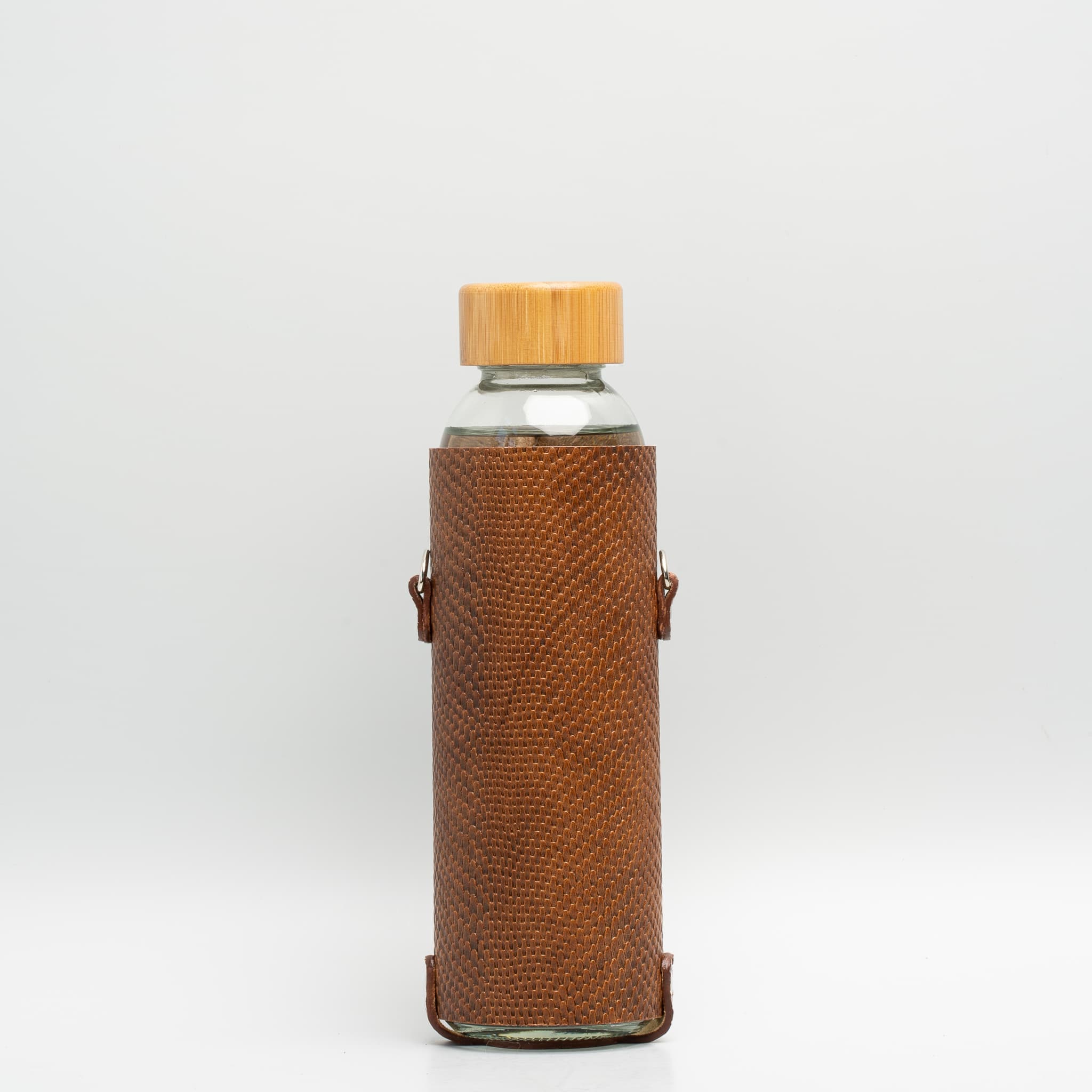Leather water bottle holder featuring a glass bottle, bamboo lid, and adjustable strap, designed for stylish hydration on the go.