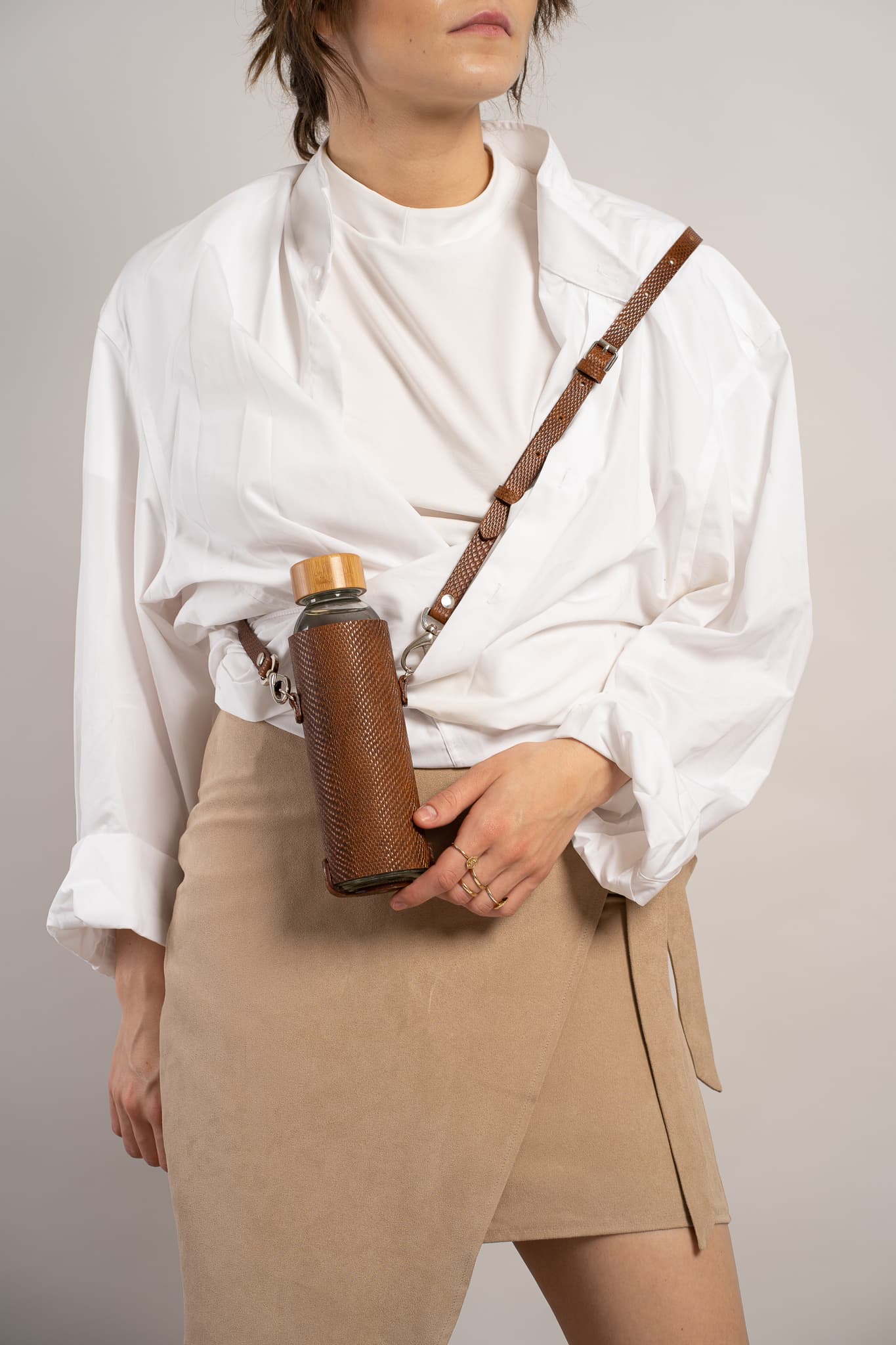 Leather water bottle holder featuring a glass bottle, bamboo lid, and adjustable strap, designed for stylish hydration on the go.