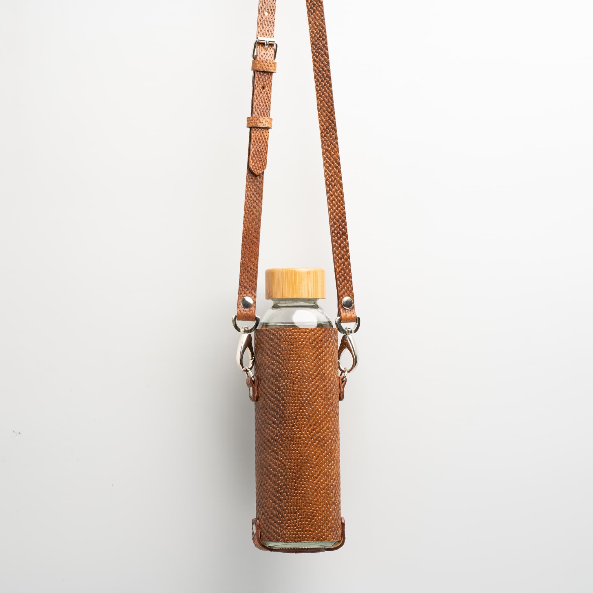 Leather water bottle holder featuring a glass bottle, bamboo lid, and adjustable strap, designed for stylish hydration on the go.
