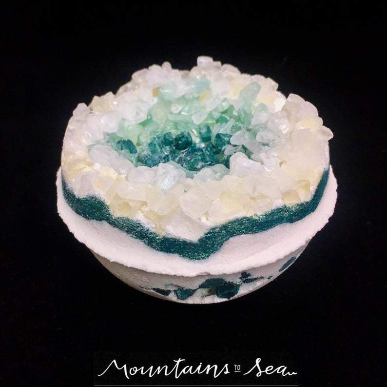 Artisan Emerald Geo Vegan Bath Bomb in a vibrant green color, resembling a geode, surrounded by natural elements like leaves and stones.