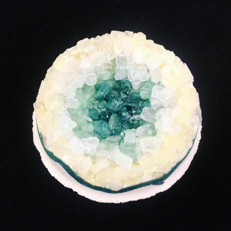Artisan Emerald Geo Vegan Bath Bomb in a vibrant green color, resembling a geode, surrounded by natural elements like leaves and stones.