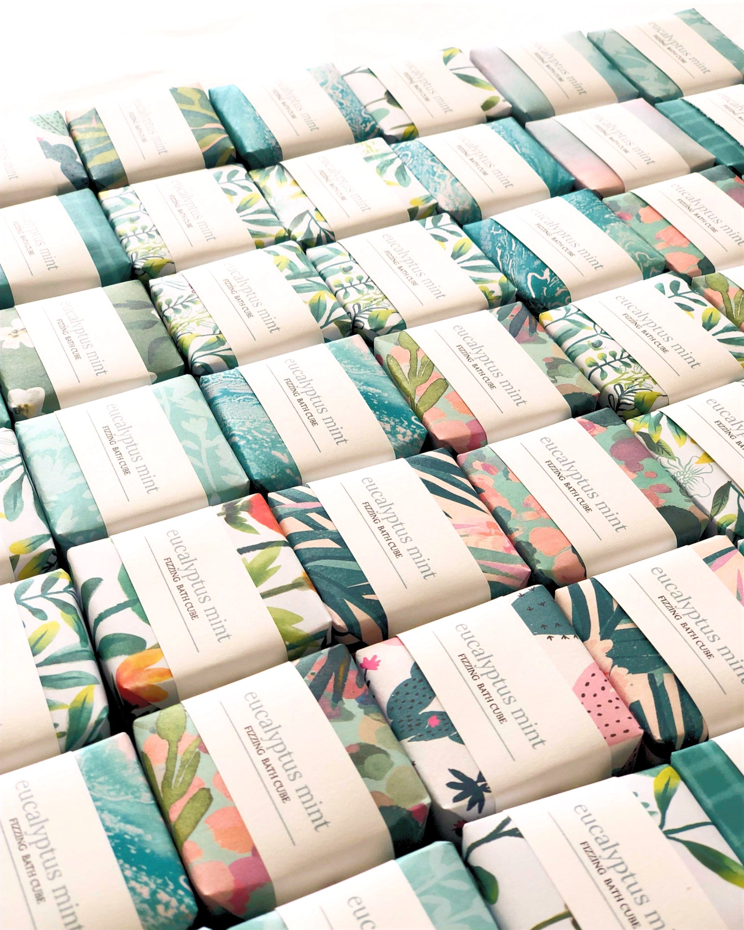 Eucalyptus Mint Bath Cube fizzing in a bathtub, surrounded by fresh eucalyptus leaves and mint sprigs.