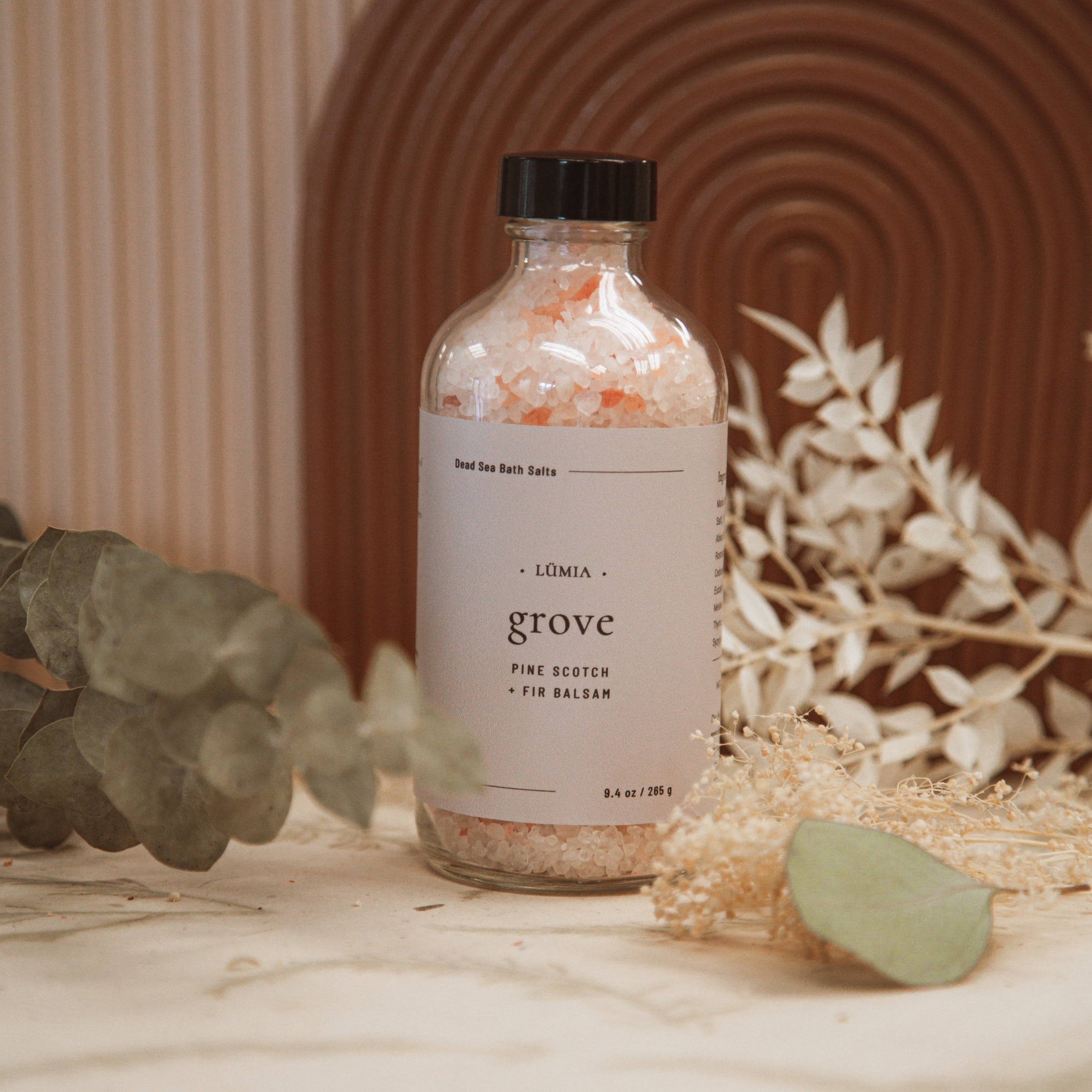 Grove Bath Salts in a clear jar with wooden lid, surrounded by natural elements like pine branches and salt crystals.
