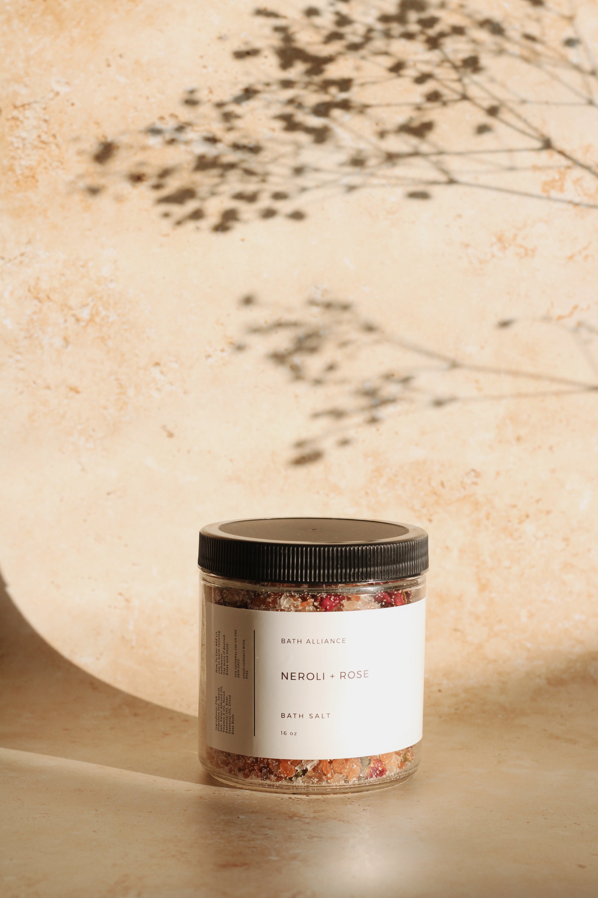 Neroli + Rose Bath Salt in a clear jar with dried rose buds, showcasing its luxurious texture and natural ingredients.