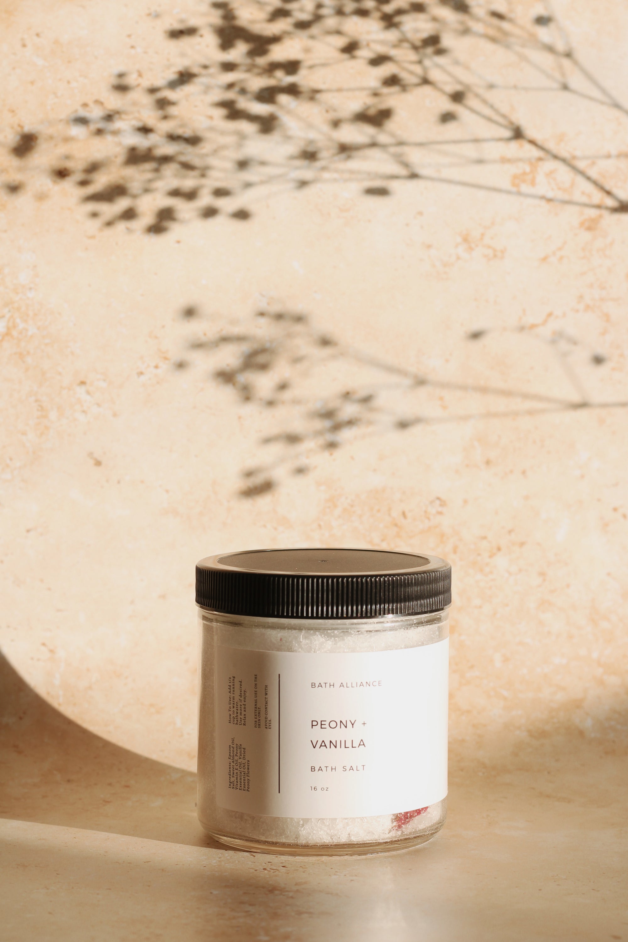 A jar of Peony + Vanilla Bath Salt with dried peony petals, showcasing its natural ingredients and luxurious scent.