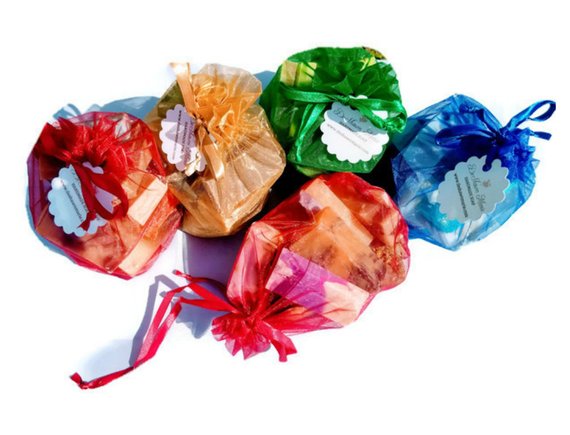 A vibrant assortment of handmade vegan soaps in jewel tones, showcasing various shapes and sizes in a decorative bag.