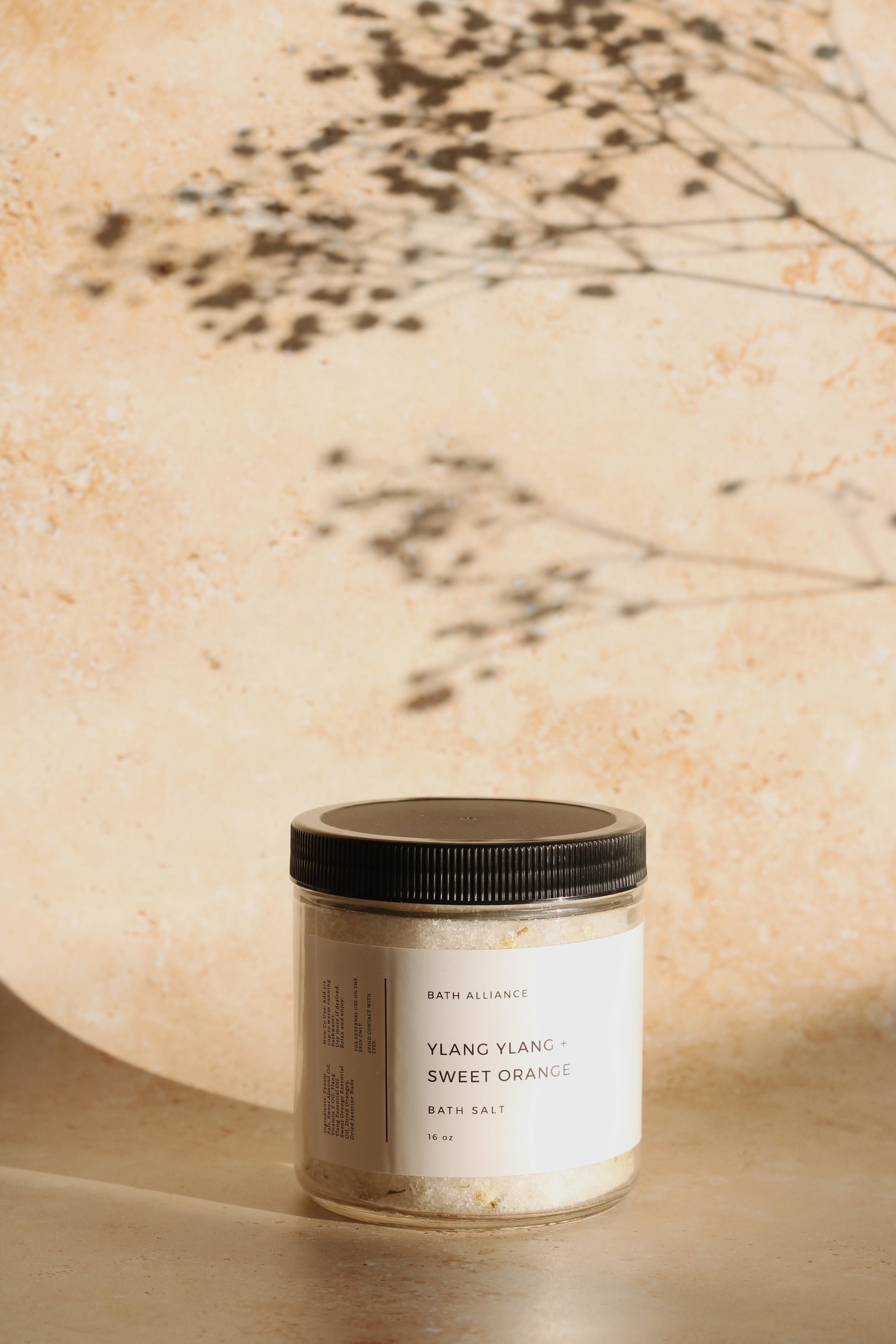 A jar of Ylang Ylang + Sweet Orange Bath Salt with dried orange slices and jasmine flower buds, showcasing its luxurious and natural ingredients.