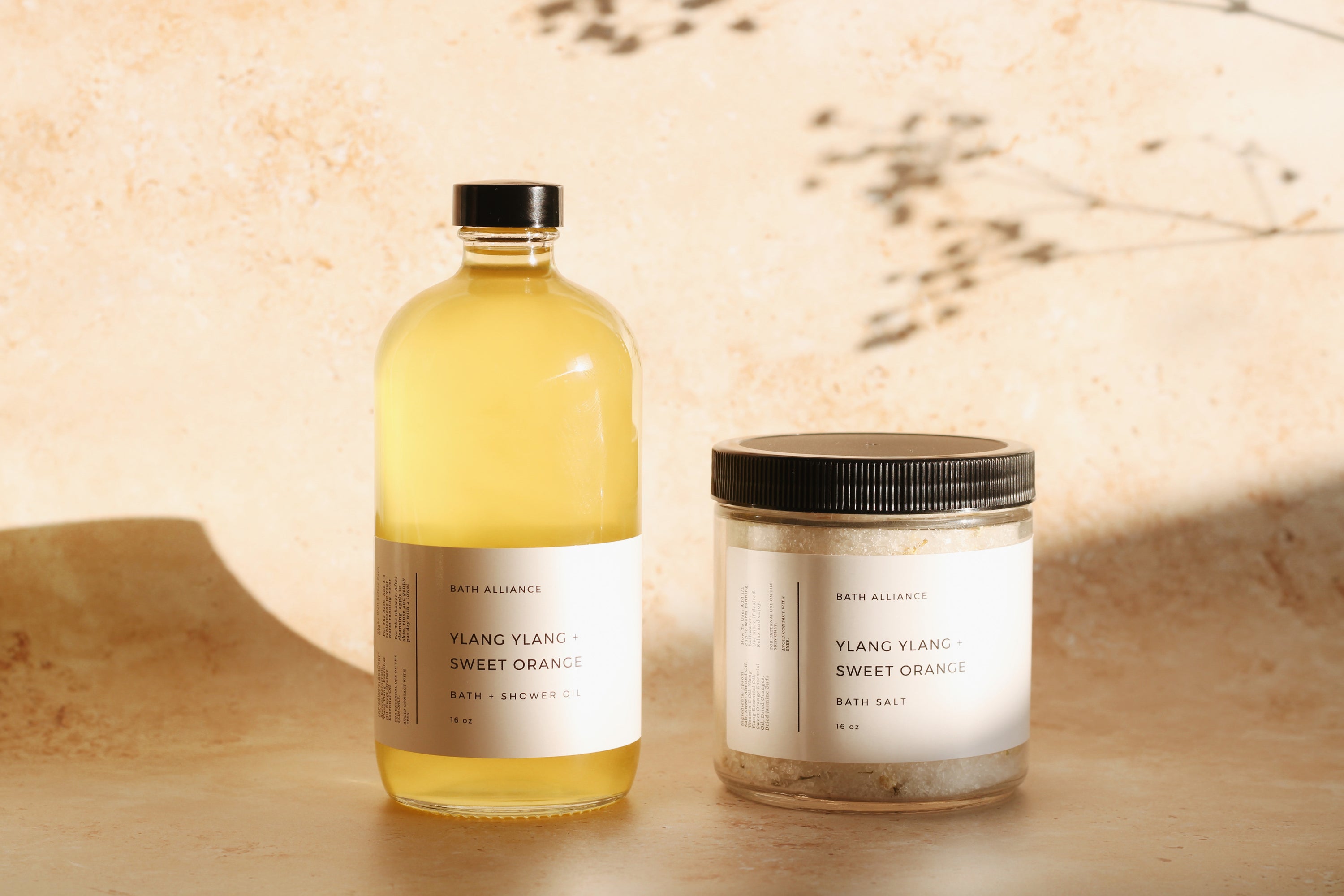 Ylang Ylang + Sweet Orange Bath Set featuring bath salt and shower oil in elegant jars, showcasing natural ingredients.