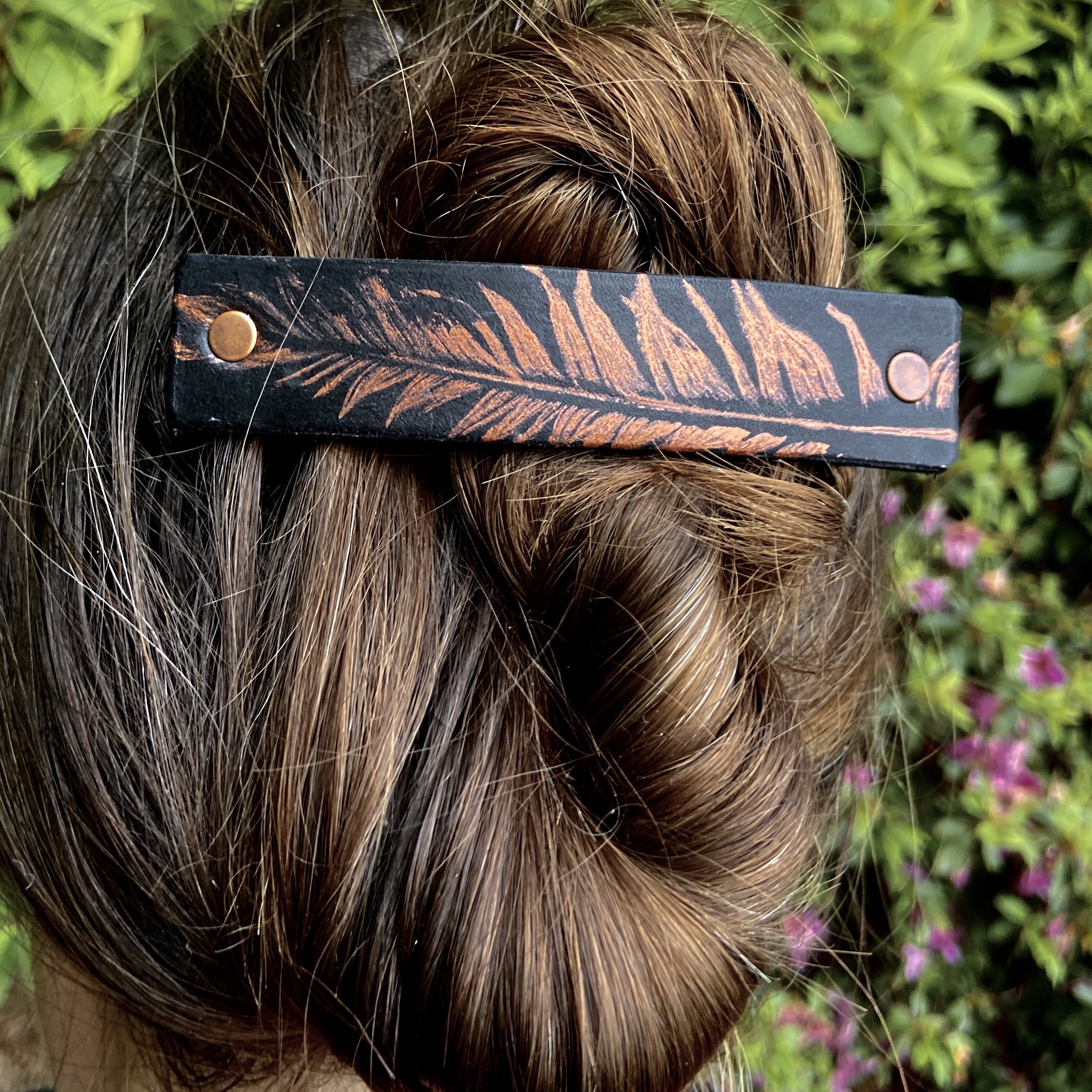 Copper feather design on a black leather barrette and matching earrings, showcasing unique craftsmanship and style.