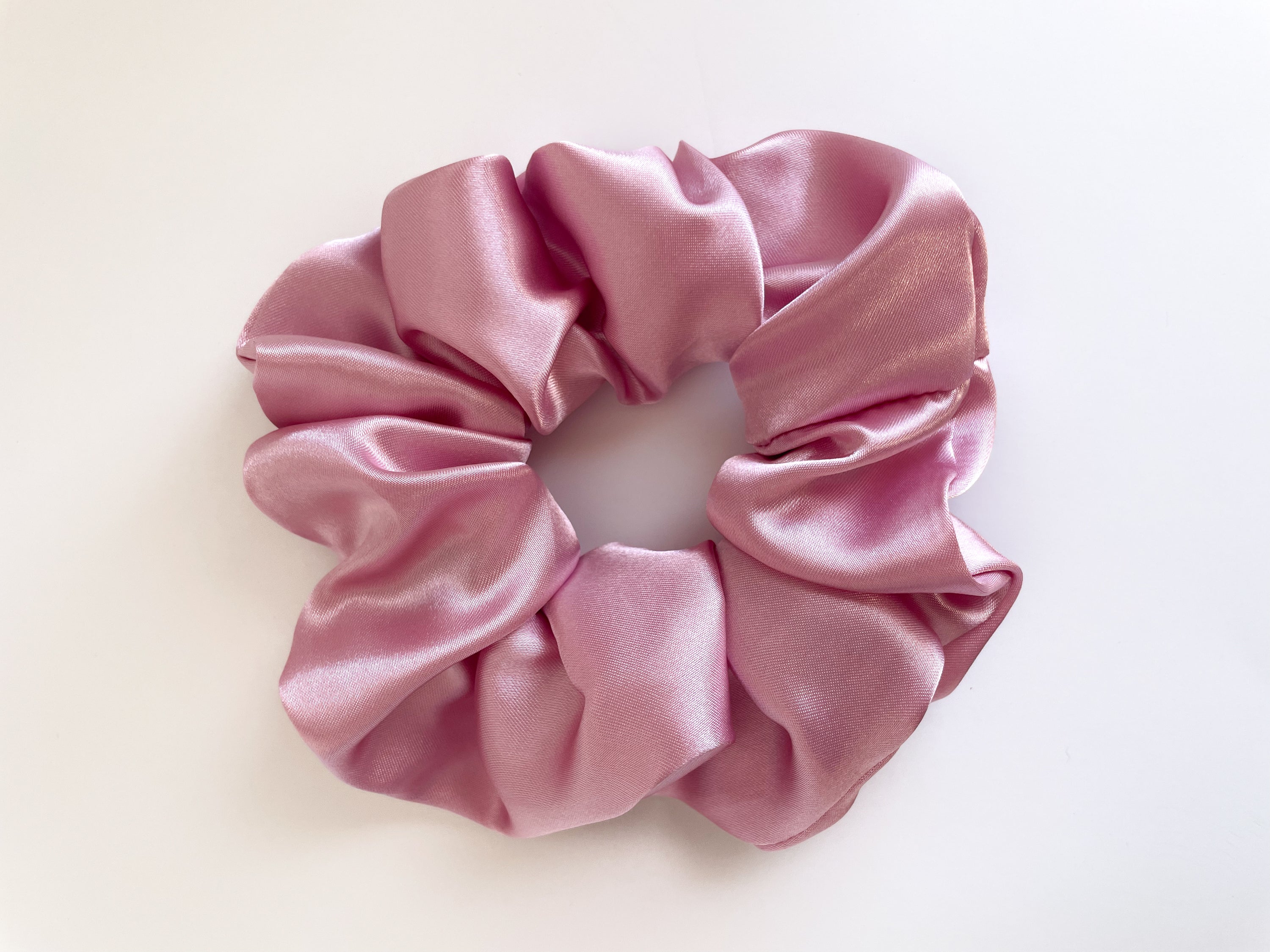 A vibrant pink lemonade satin scrunchie, soft and stylish, perfect for securing hair without causing damage.