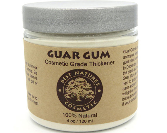 A fine powder of Guar Gum, a natural thickener derived from the guar plant, displayed in a small bowl with a wooden spoon, showcasing its texture and color.