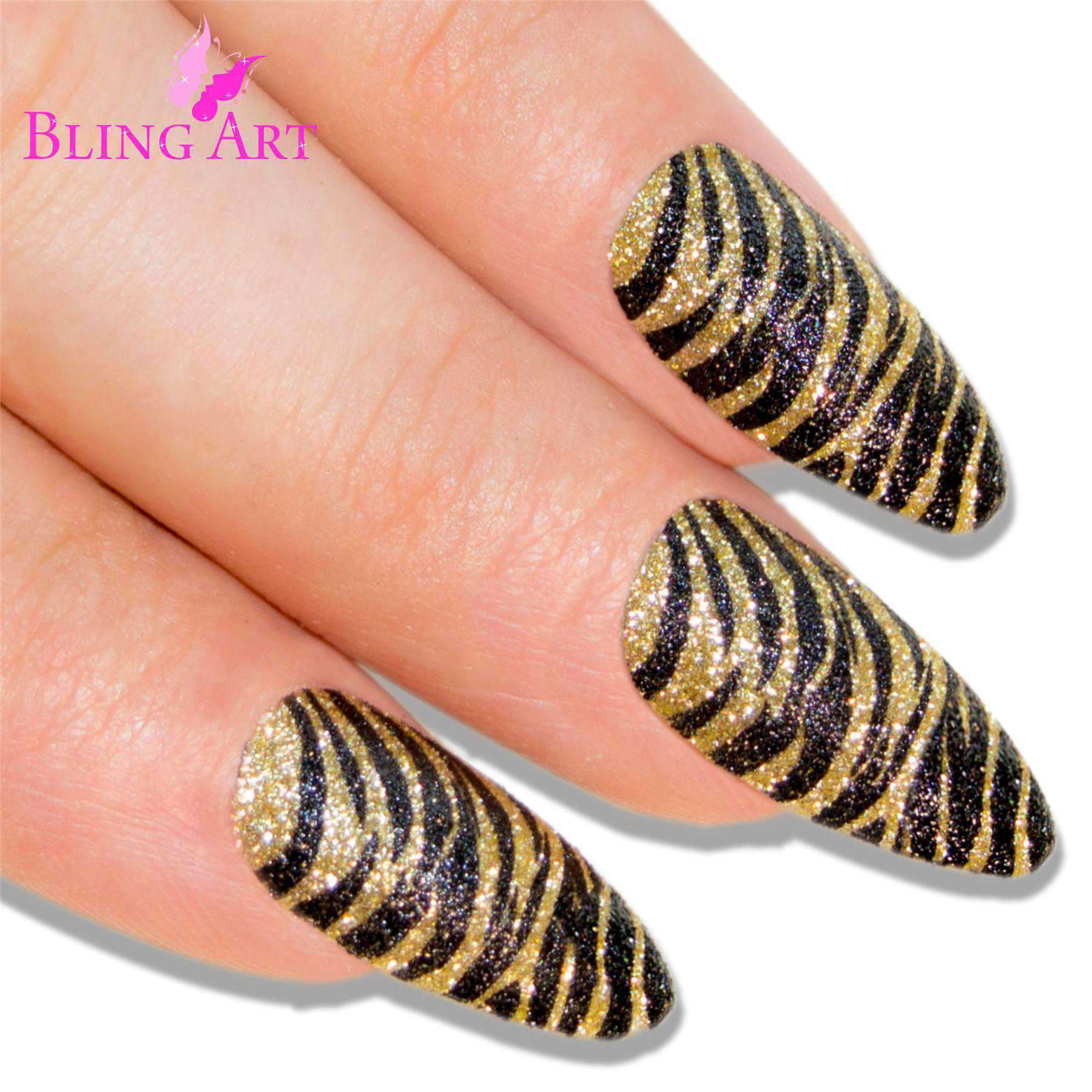 A set of 24 long almond stiletto false nails in black and gold glitter design, accompanied by a glue stick, nail file, and cuticle stick.