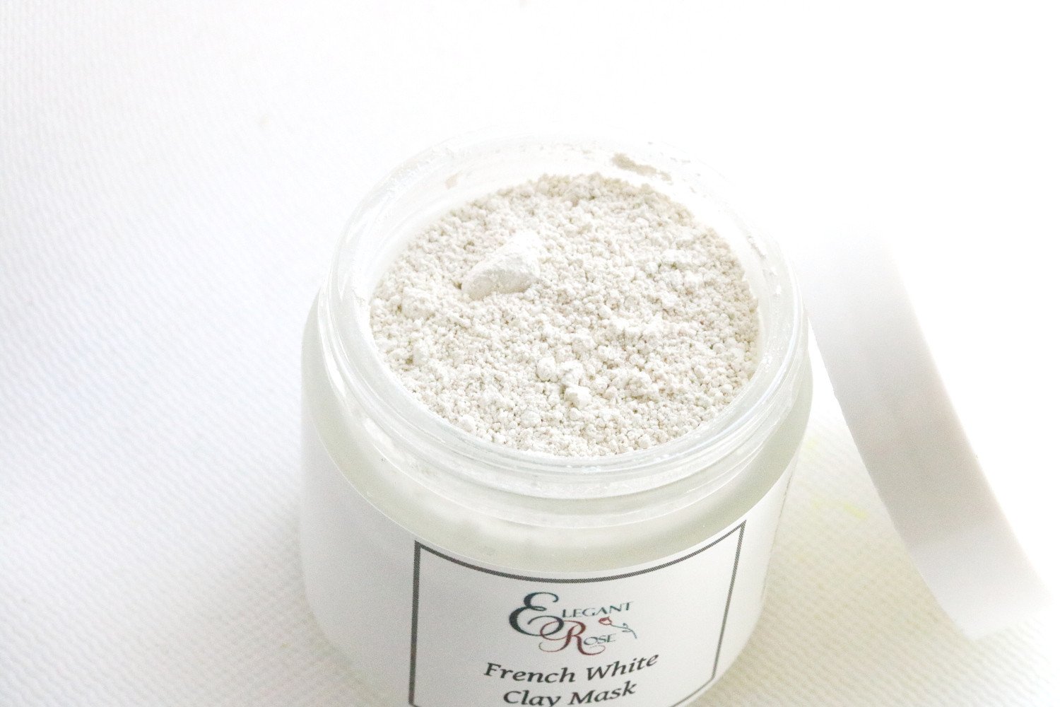 A 2-ounce glass jar of French White Clay Mask with a smooth, creamy texture, surrounded by natural botanical ingredients.