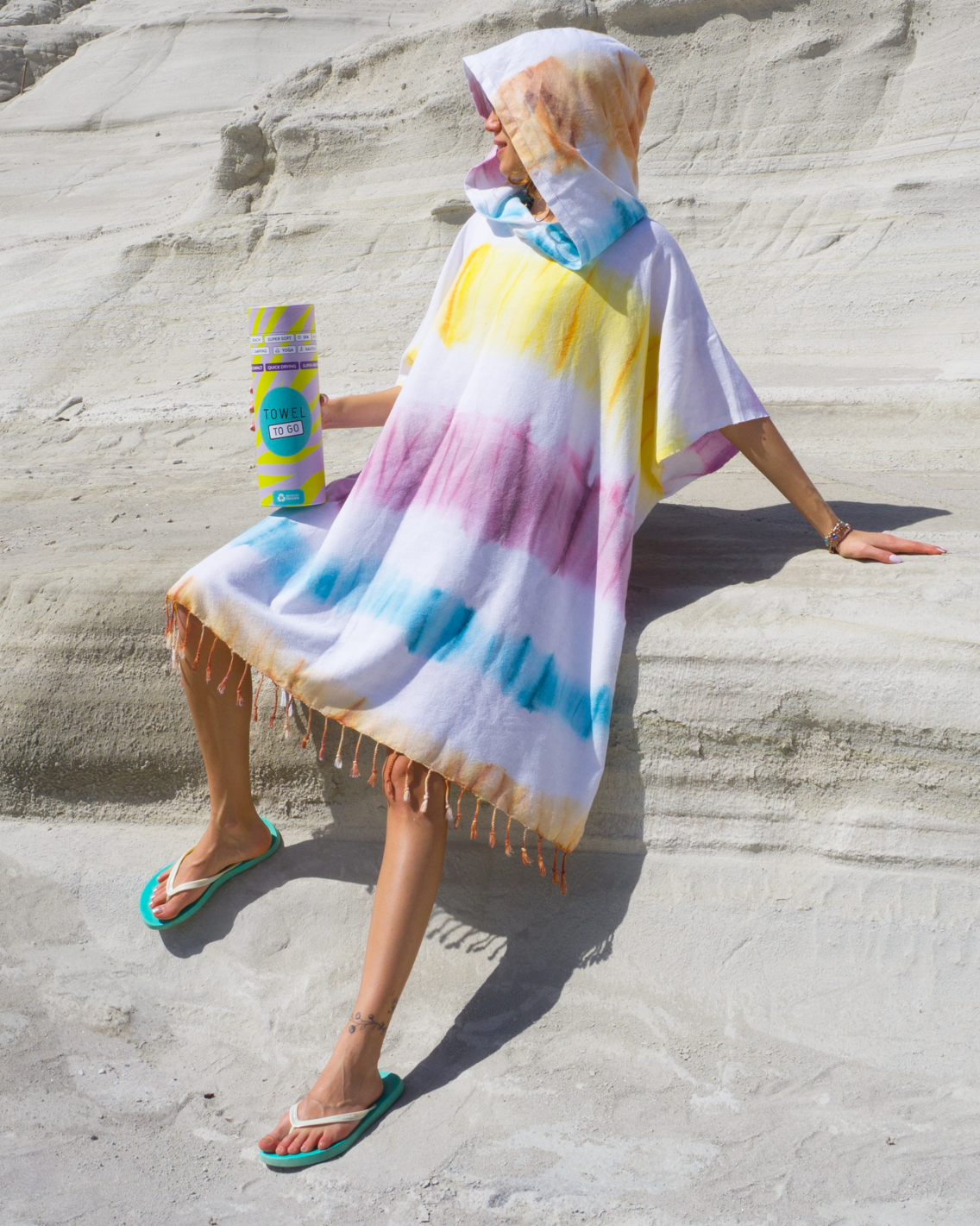 A vibrant purple and blue tie dye hooded beach poncho displayed in a sunny beach setting, showcasing its unique patterns and relaxed fit.