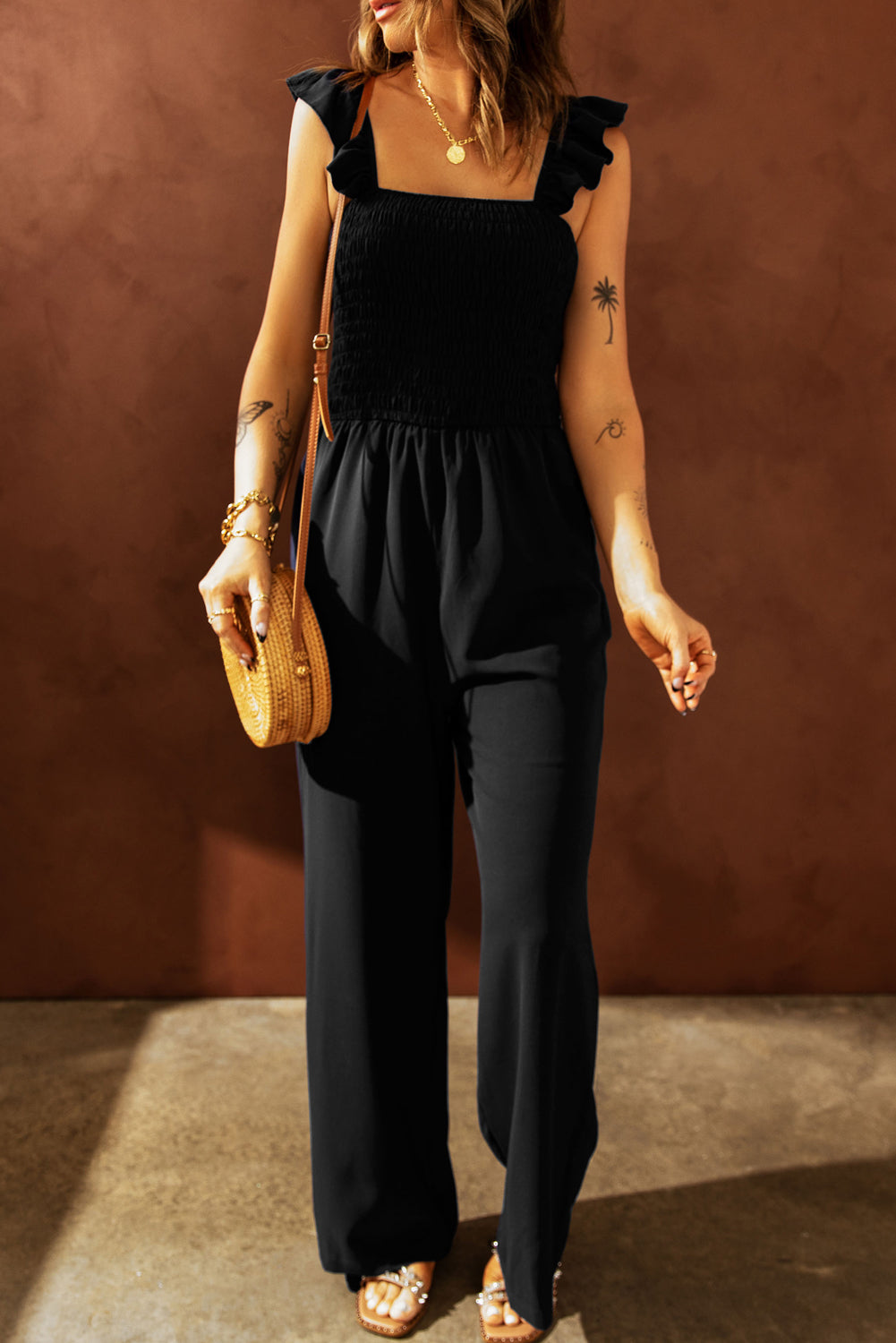 A stylish black jumpsuit featuring flutter sleeves, a smocked bodice, and wide leg bottoms, perfect for any occasion.