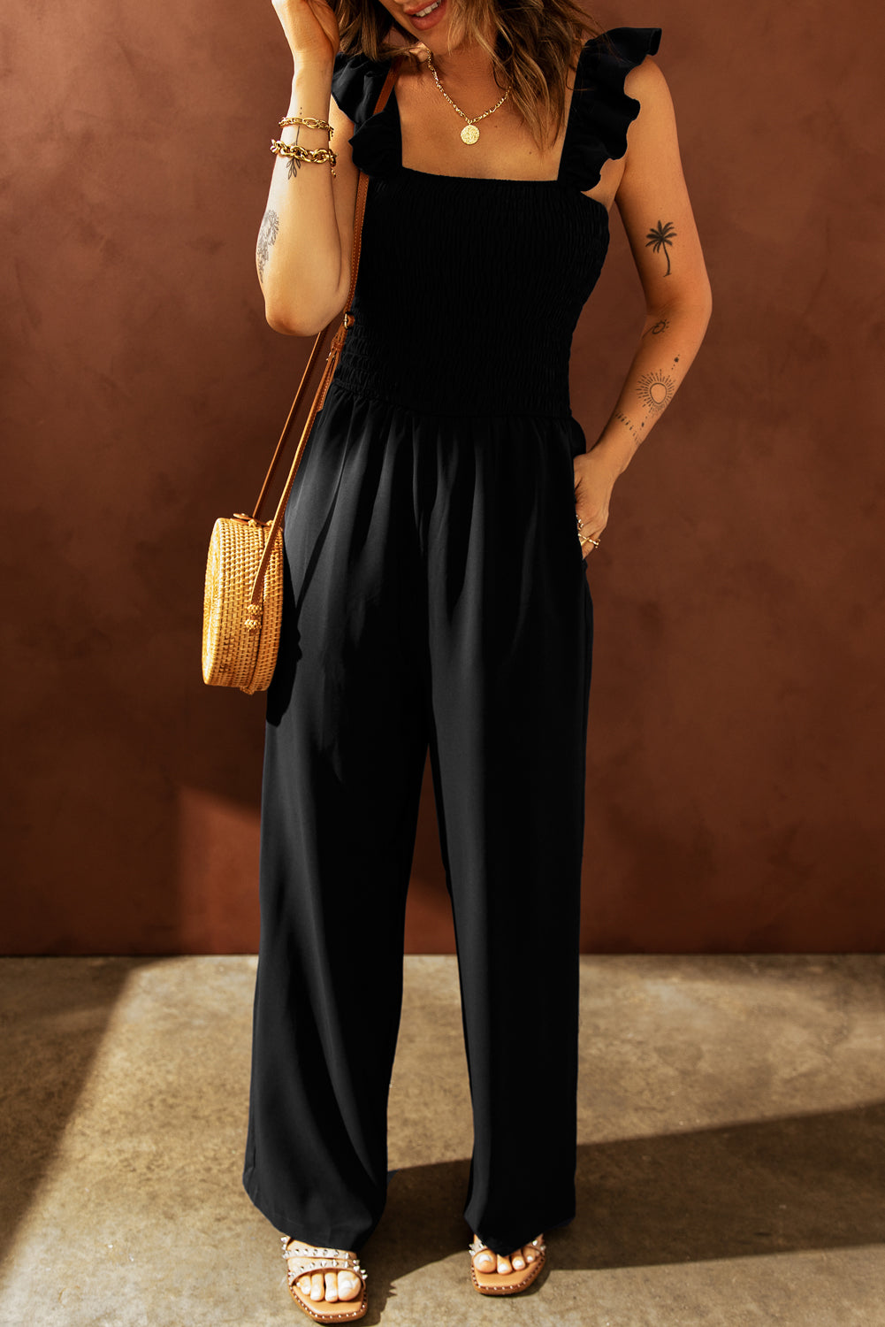 A stylish black jumpsuit featuring flutter sleeves, a smocked bodice, and wide leg bottoms, perfect for any occasion.