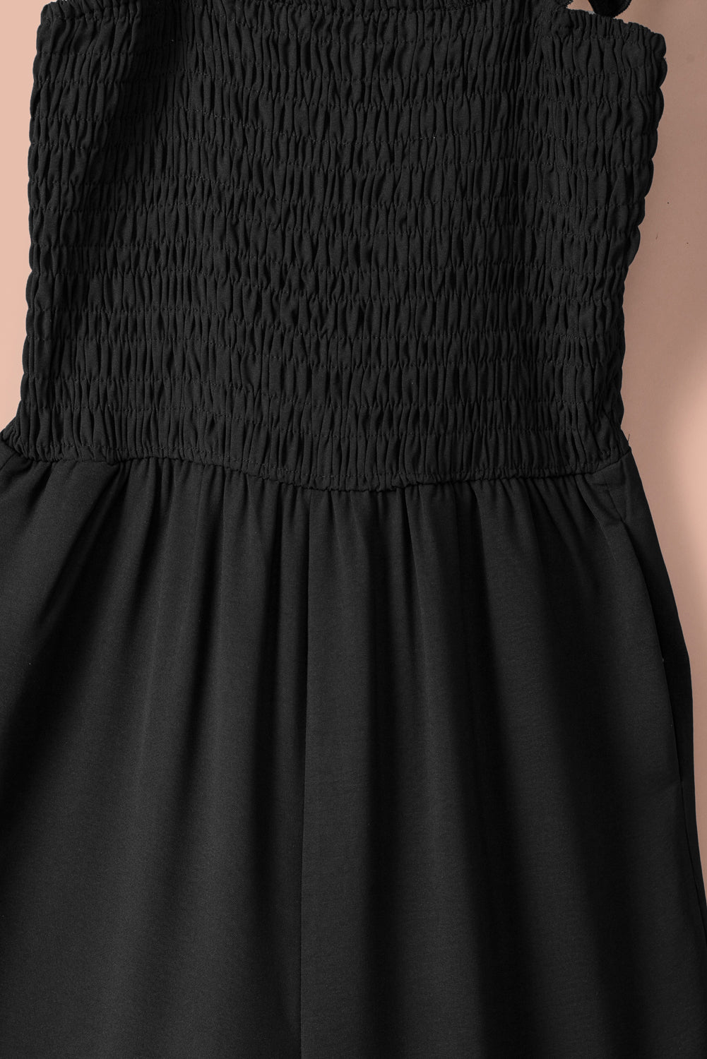 A stylish black jumpsuit featuring flutter sleeves, a smocked bodice, and wide leg bottoms, perfect for any occasion.