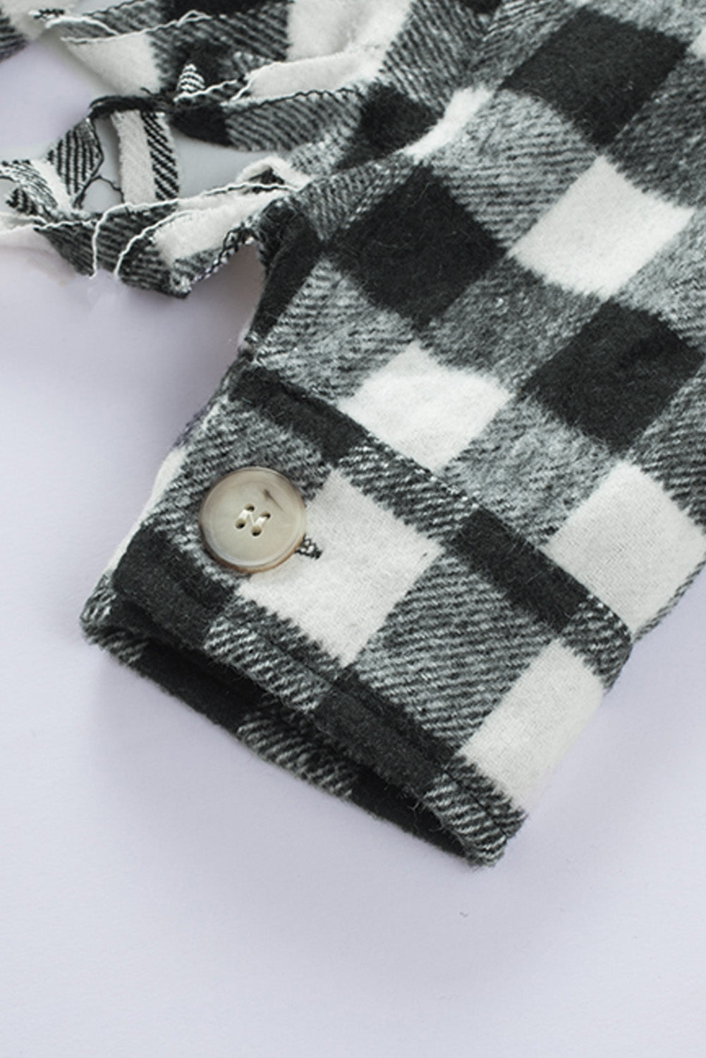 Black fringed plaid print shacket featuring a classic black and white pattern, collared neckline, and stylish fringe details on sleeves.
