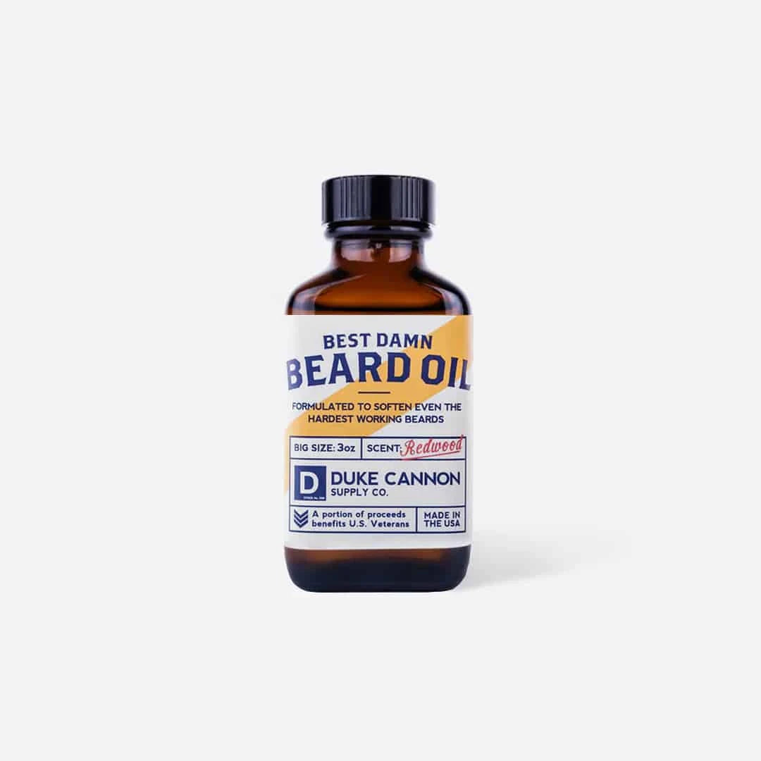 Duke Cannon Best Damn Beard Oil in Redwood bottle with a rustic background, showcasing its premium natural ingredients.