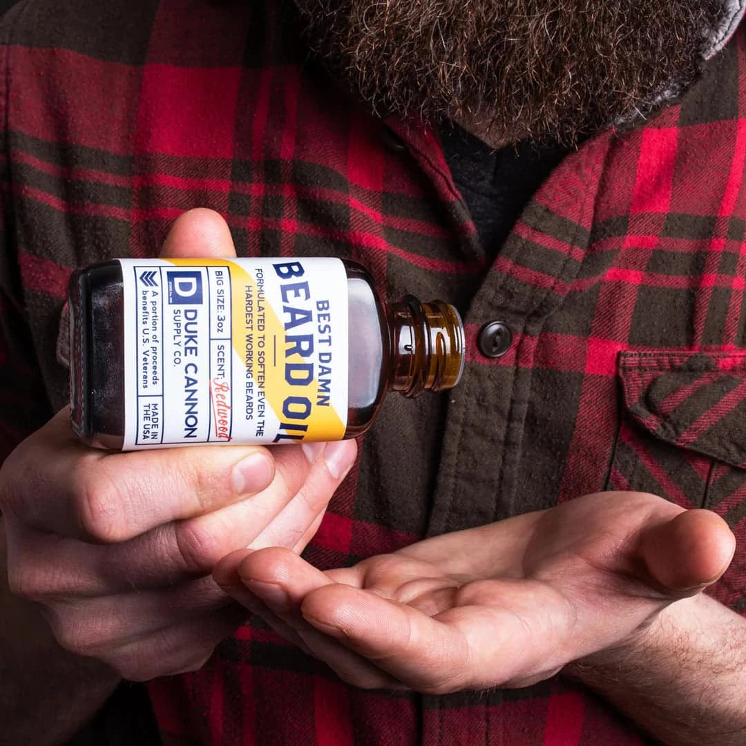 Duke Cannon Best Damn Beard Oil in Redwood bottle with a rustic background, showcasing its premium natural ingredients.