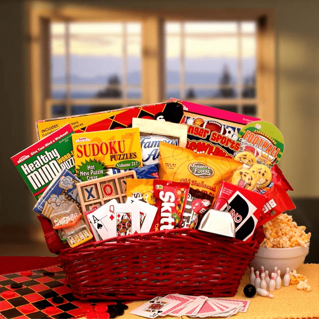 A vibrant Fun & Games Gift Basket filled with games and sweet treats, including cookies, candies, and puzzle books, presented in a glossy red basket.