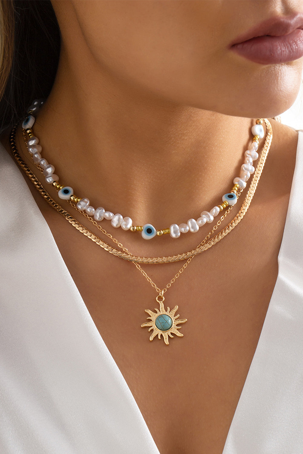 A multi-layered pendant necklace featuring turquoise and pearl beads with a gold sun pendant, elegantly displayed on a soft background.