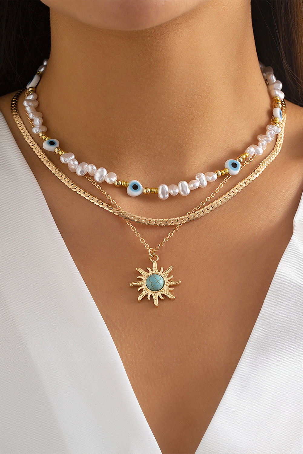 A multi-layered pendant necklace featuring turquoise and pearl beads with a gold sun pendant, elegantly displayed on a soft background.