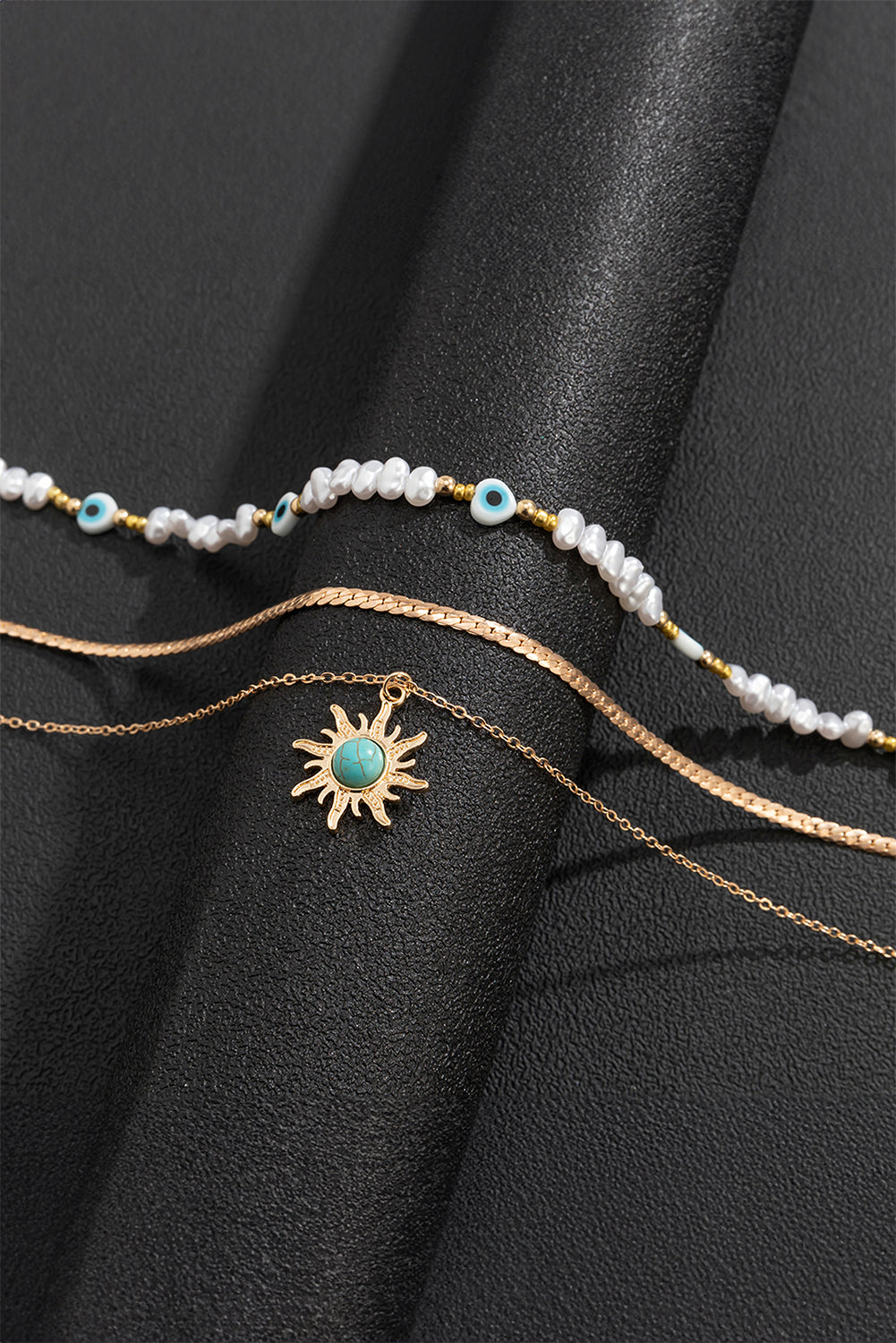 A multi-layered pendant necklace featuring turquoise and pearl beads with a gold sun pendant, elegantly displayed on a soft background.