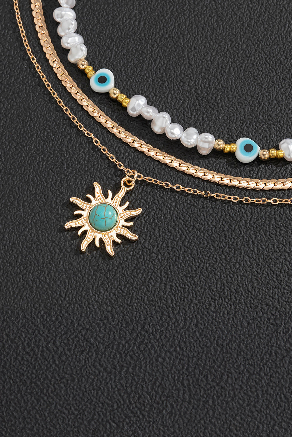 A multi-layered pendant necklace featuring turquoise and pearl beads with a gold sun pendant, elegantly displayed on a soft background.