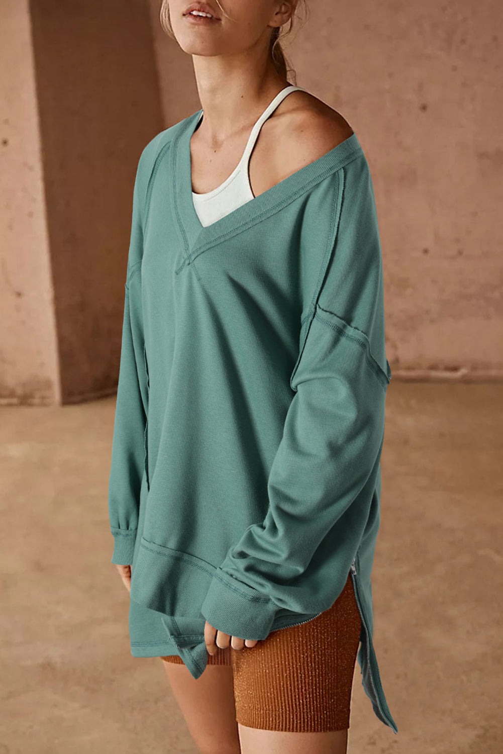 A stylish green high low sweatshirt featuring a V-neck and exposed seam detailing, perfect for casual wear.