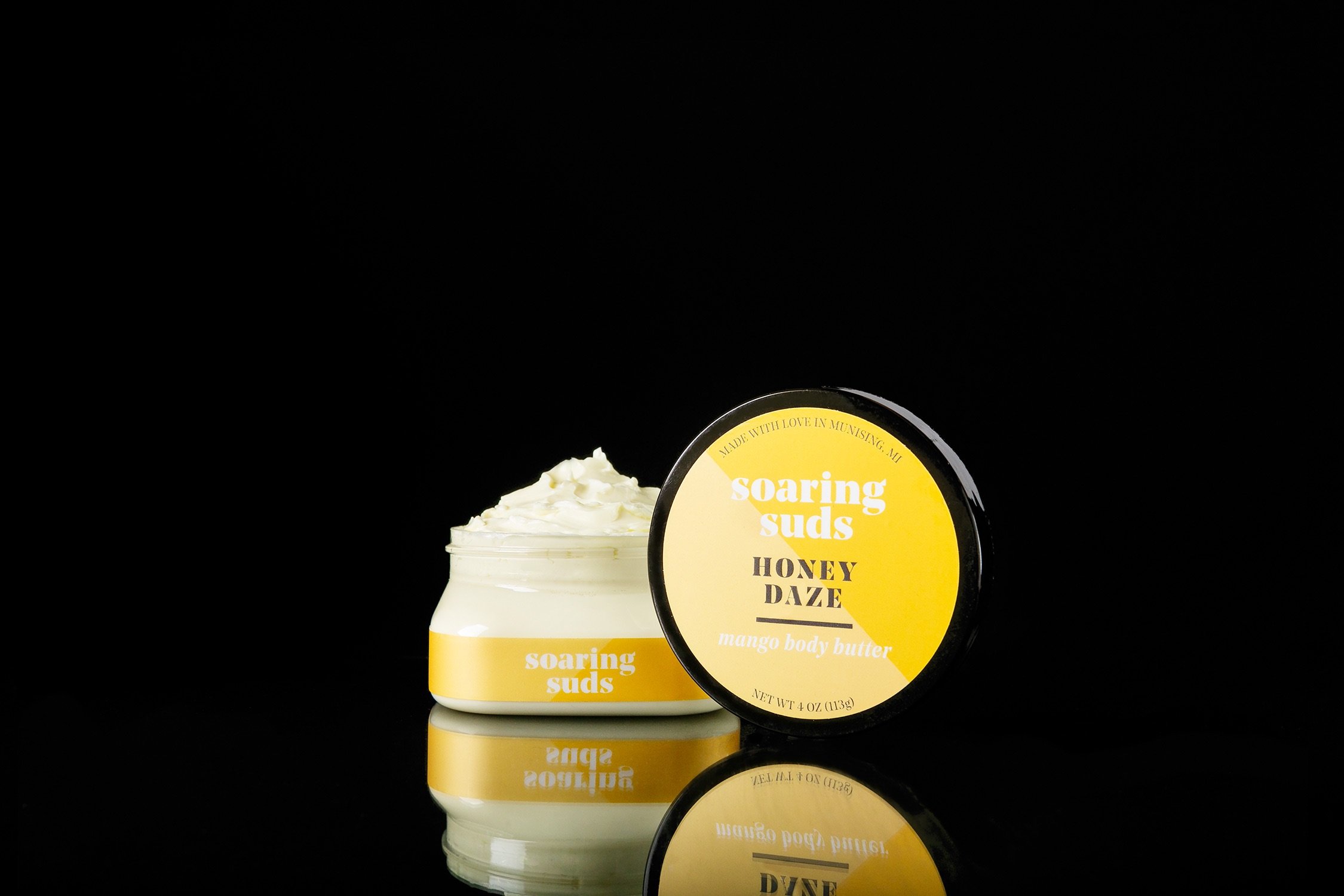 A 4 oz jar of Honey Daze Mango Body Butter with a creamy texture, showcasing its natural ingredients and vibrant packaging.