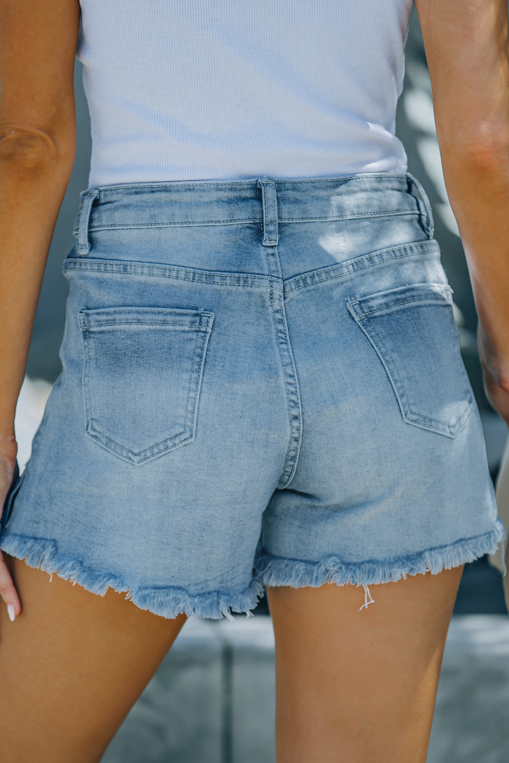 Light blue distressed ripped denim shorts with pockets, featuring a frayed hemline and high rise fit, perfect for summer wear.