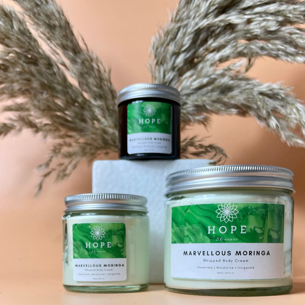 A jar of Marvellous Moringa Whipped Body Cream with a smooth, creamy texture, surrounded by Moringa leaves and Bergamot fruit.