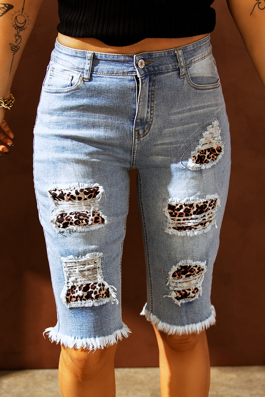 Mid-rise denim Bermuda shorts with ripped detailing and leopard patches, showcasing a trendy summer style.