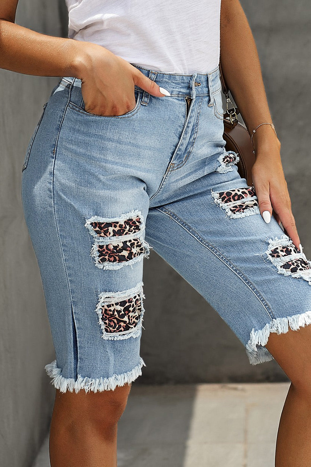 Mid-rise denim Bermuda shorts with ripped detailing and leopard patches, showcasing a trendy summer style.