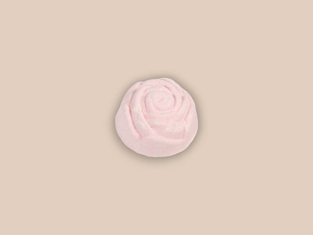 A vibrant Mini Rose Bath Bomb in a pink hue, surrounded by rose petals, showcasing its luxurious coconut rose scent.