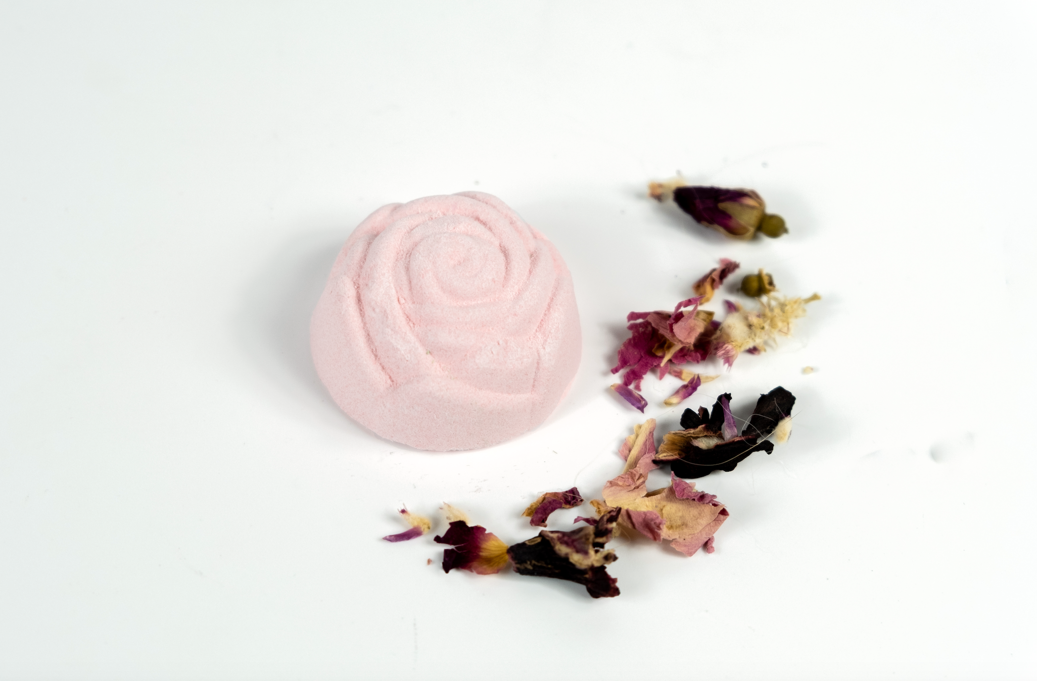 A vibrant Mini Rose Bath Bomb in a pink hue, surrounded by rose petals, showcasing its luxurious coconut rose scent.