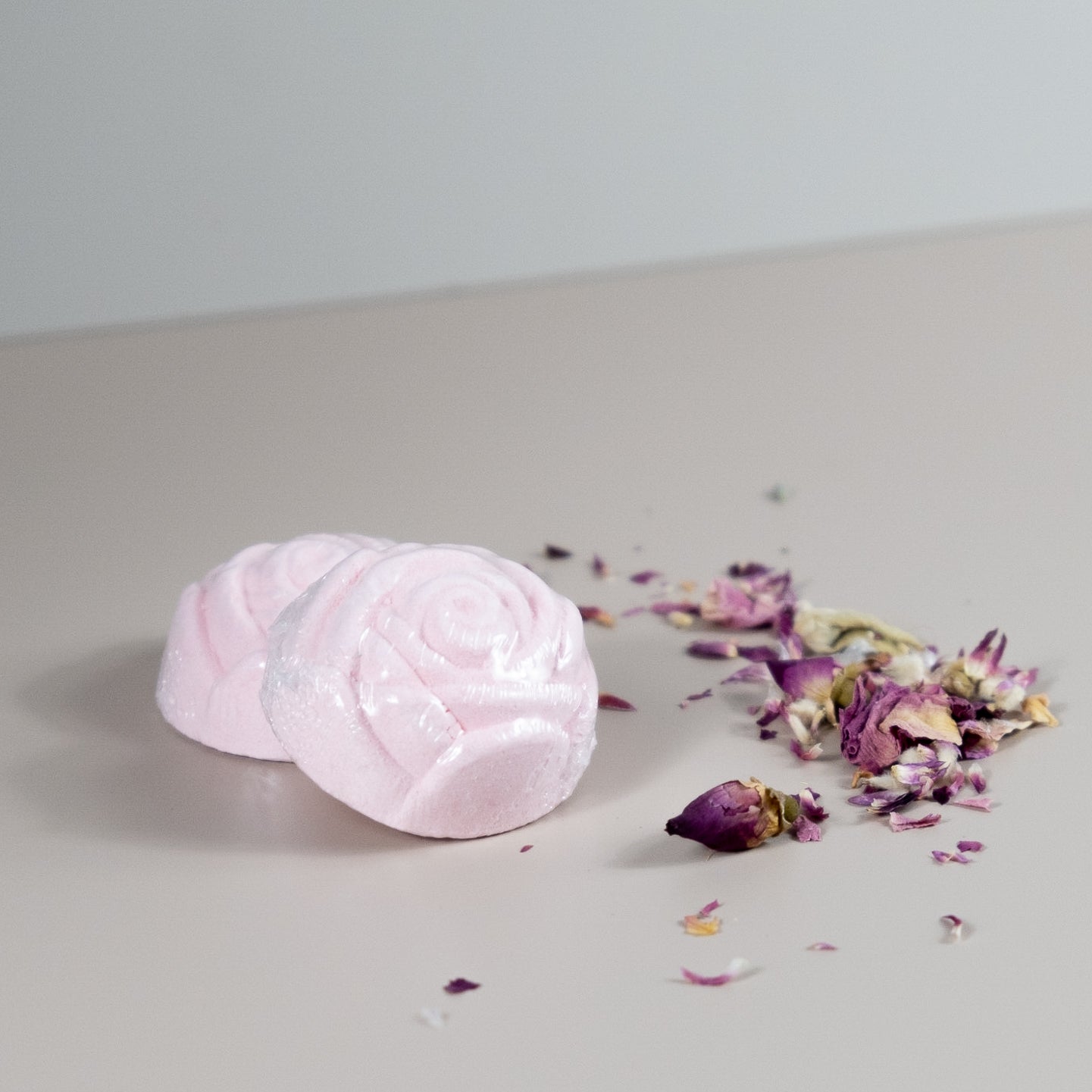A vibrant Mini Rose Bath Bomb in a pink hue, surrounded by rose petals, showcasing its luxurious coconut rose scent.