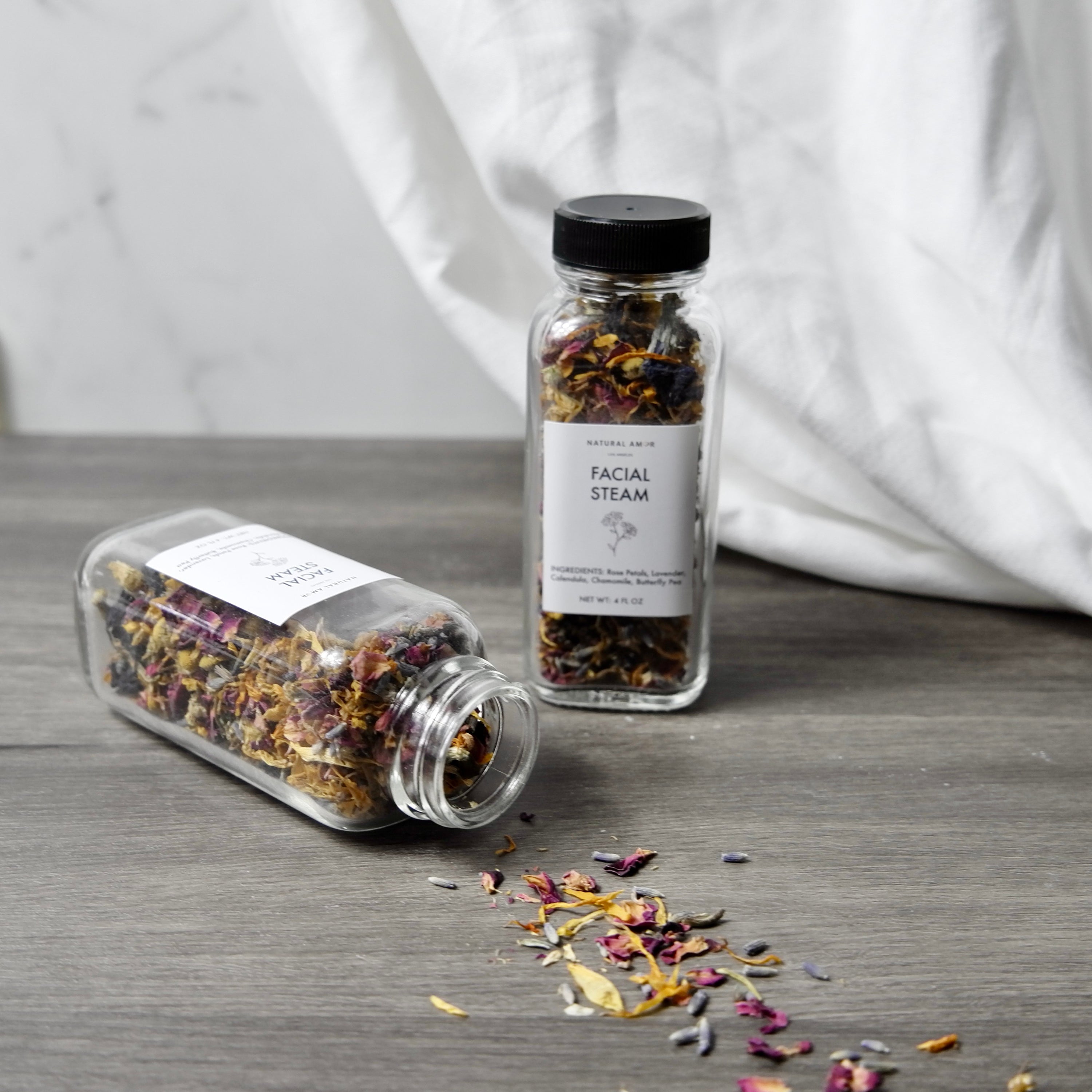 A 4oz glass jar filled with a colorful blend of organic herbs and botanicals for facial steaming, including rose petals and lavender.