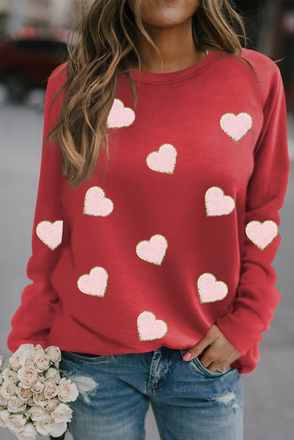 A cozy red pullover sweatshirt featuring heart-shaped chenille patches with glittery edges, perfect for Valentine's Day.