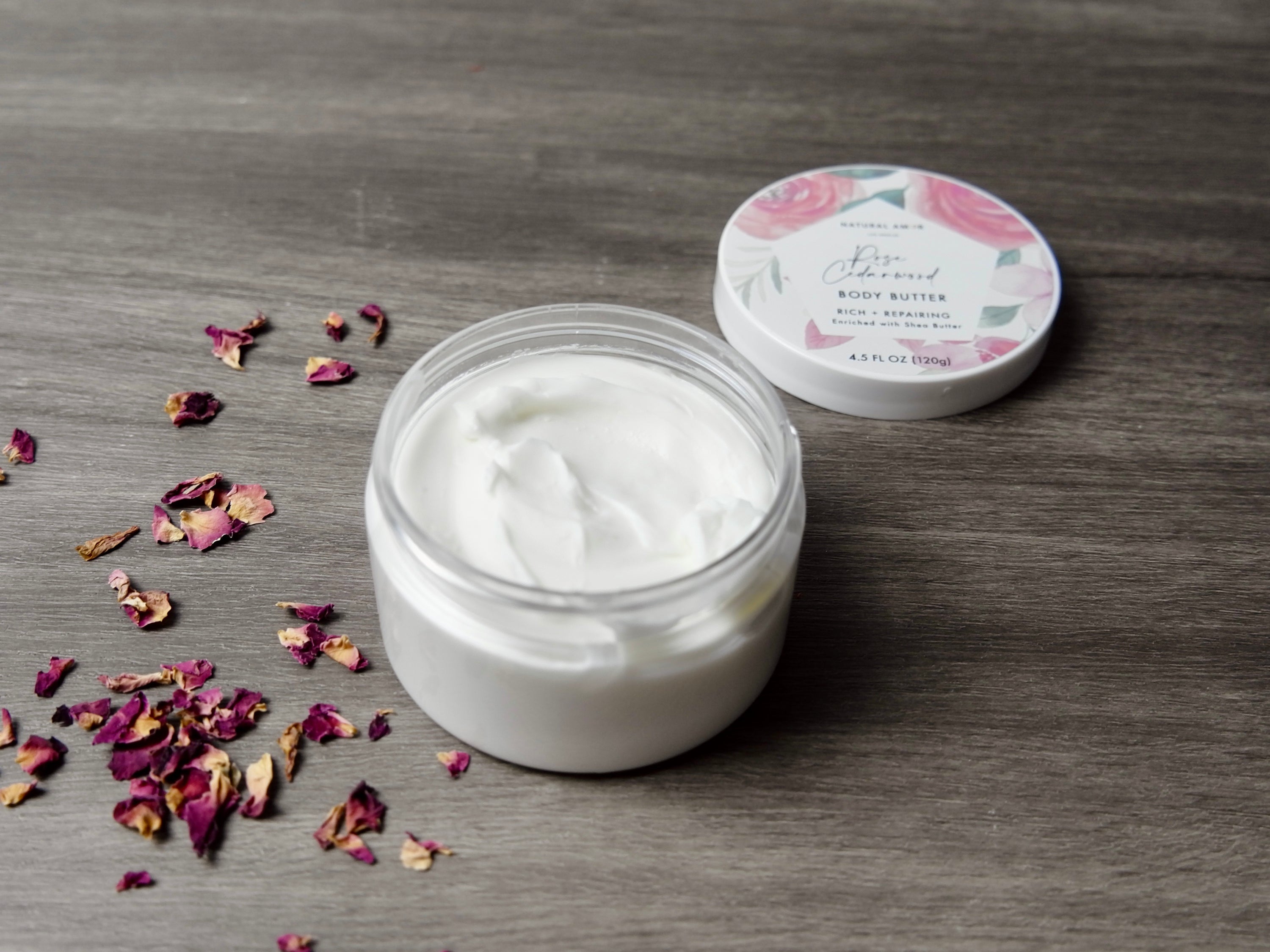 A jar of Rose Cedarwood Emulsified Body Butter with a creamy texture, surrounded by natural ingredients like shea butter and essential oils.