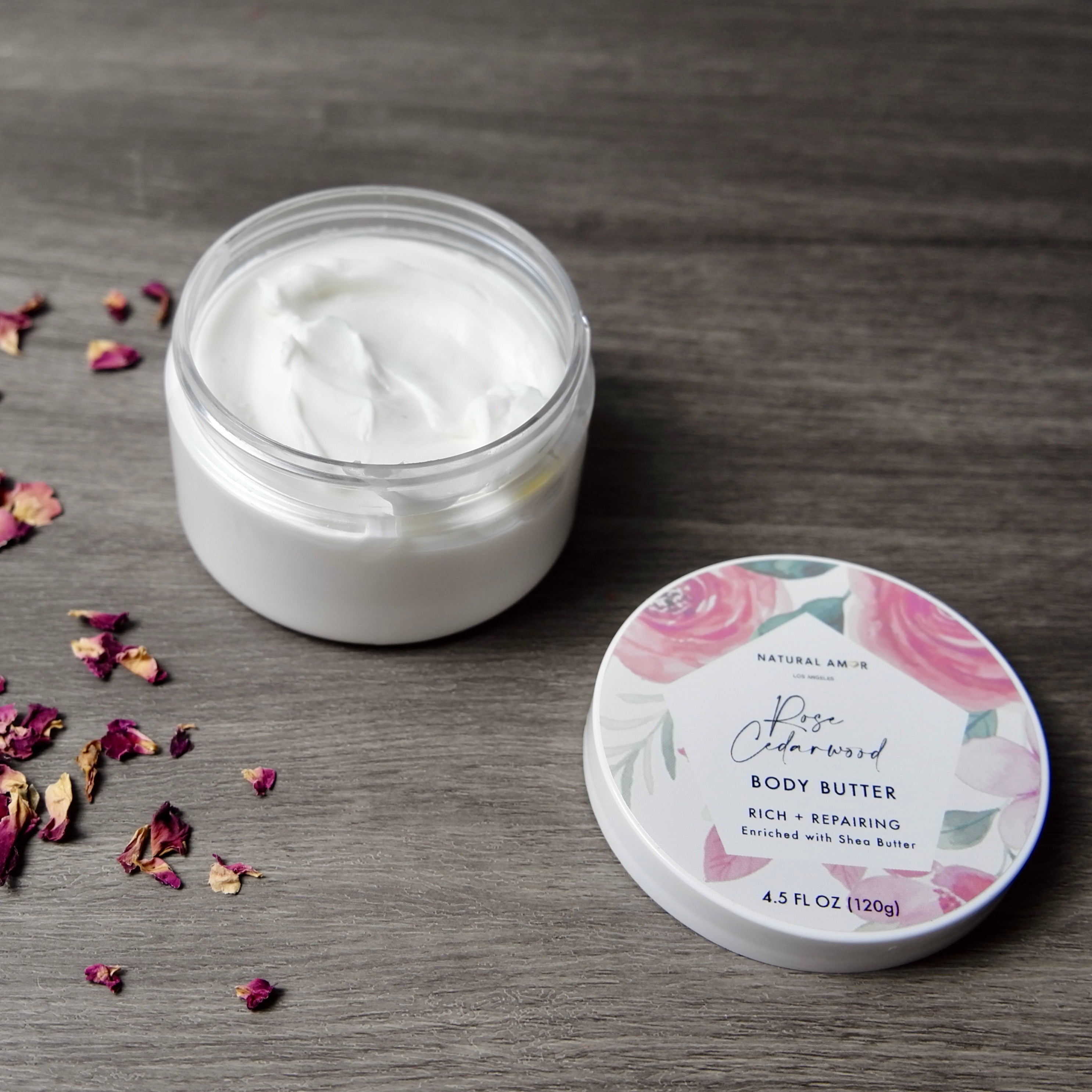 A jar of Rose Cedarwood Emulsified Body Butter with a creamy texture, surrounded by natural ingredients like shea butter and essential oils.