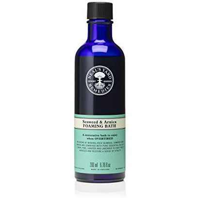 A bottle of Neal's Yard Seaweed & Arnica Foaming Bath with a soothing blue label, surrounded by seaweed and arnica flowers.