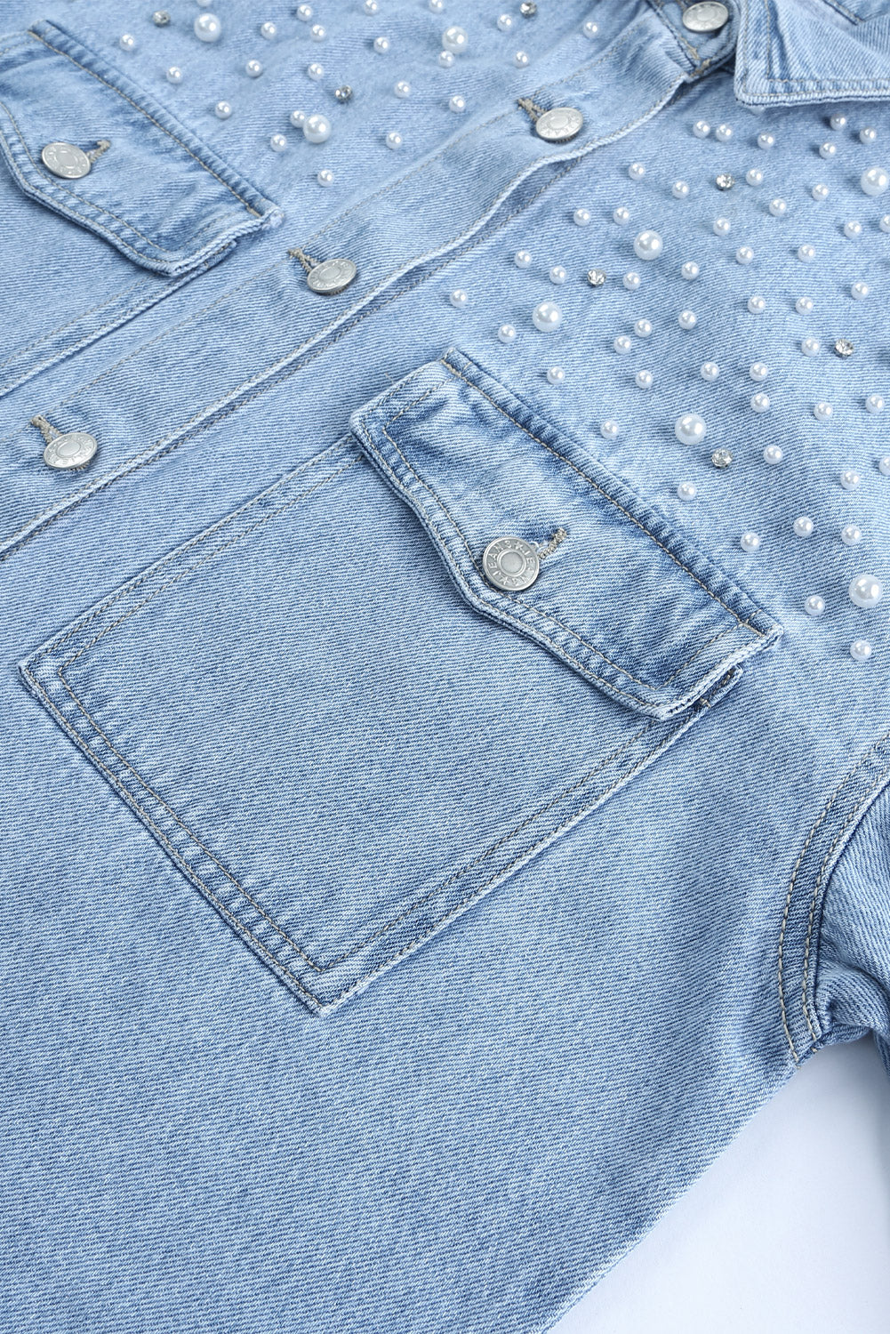Sky blue denim shacket embellished with rhinestones and pearls, featuring a raw hemline and flap pockets.