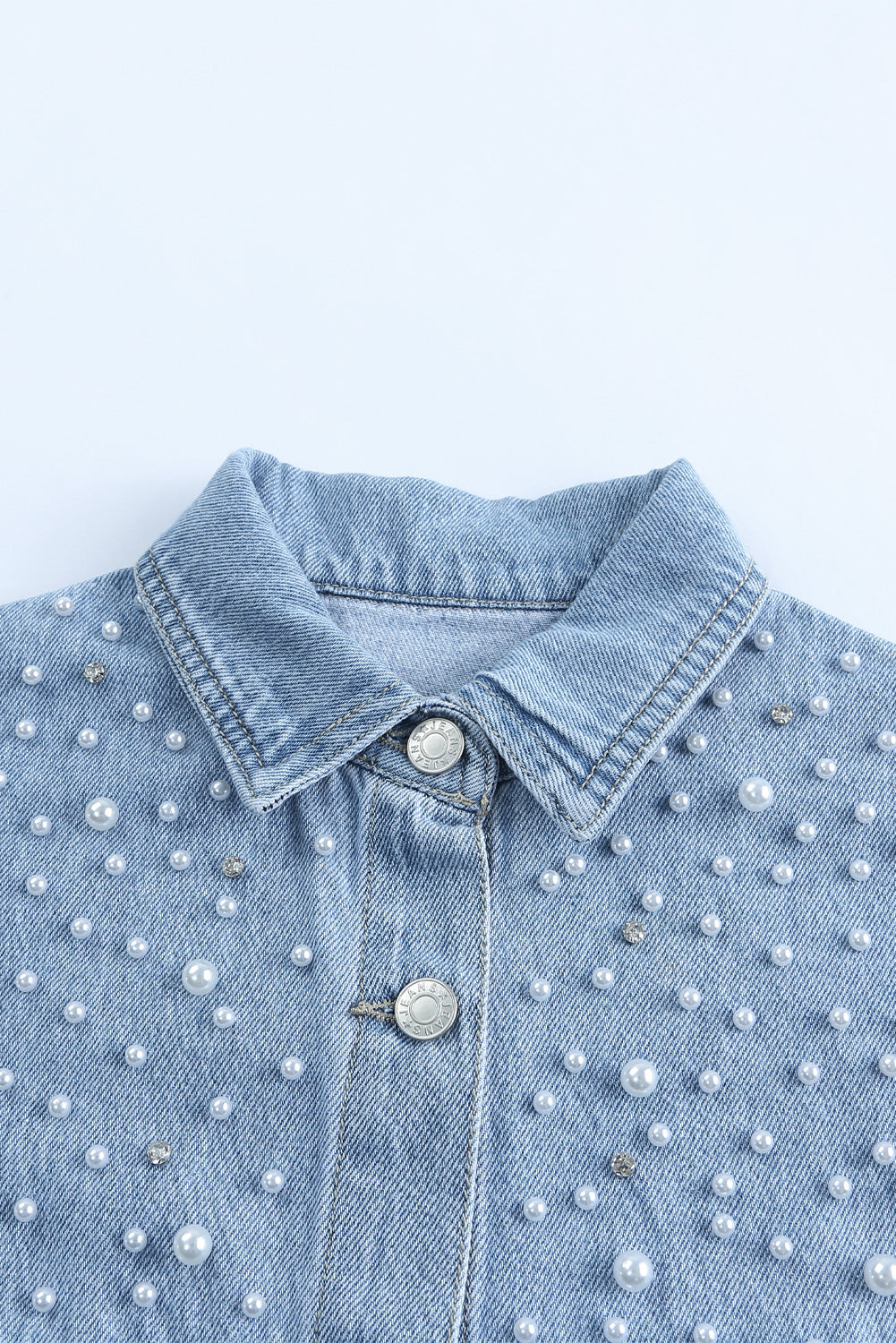 Sky blue denim shacket embellished with rhinestones and pearls, featuring a raw hemline and flap pockets.
